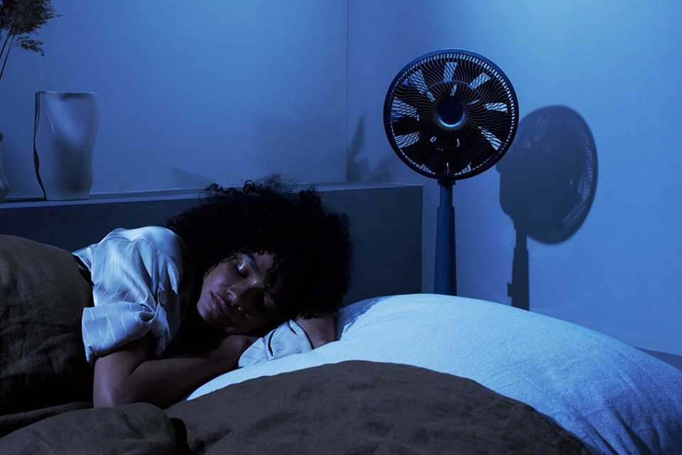 12 inch Duux Whisper Grey Pedestal Fan placed in a bedroom.