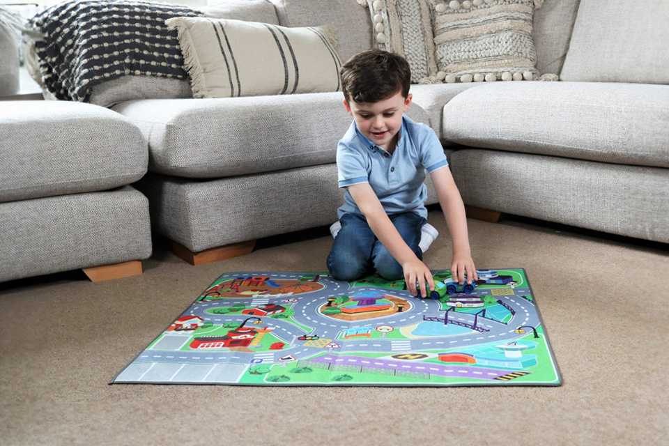 A boy playing with a Chad Valley Dual Sided toy car mat and 2 Cars.