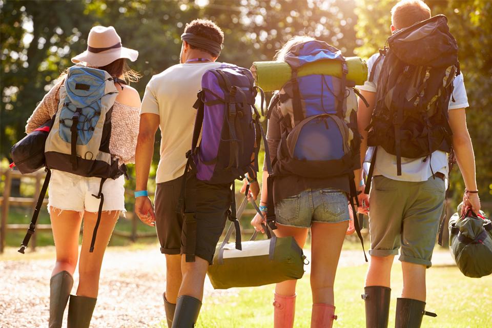 Four friends walking to a festival with rucksacks and wellies on.