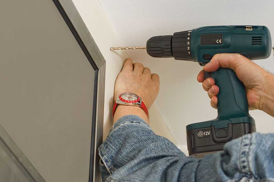 A person drilling a hole above a window to install a curtain pole.