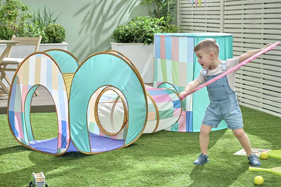 A little boy playing outdoors with a Chad Valley 3-in-1 Play Tent nearby.