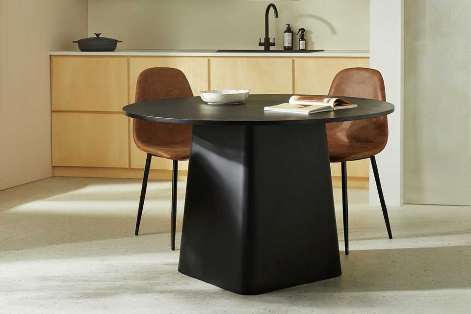 A Habitat Arelo Round 4 Seater black Dining Table and two brown chairs in a dining room.