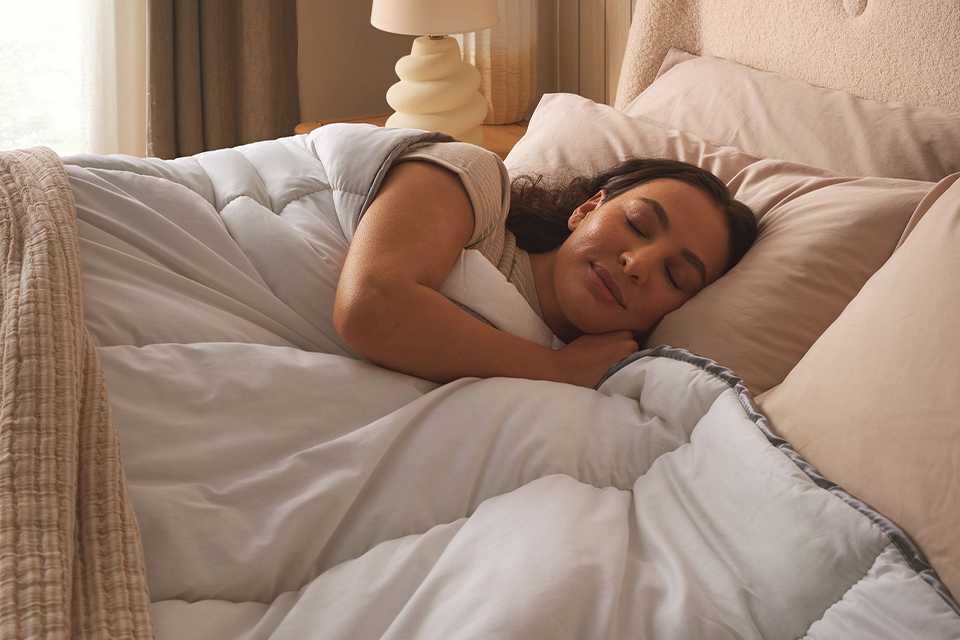 A woman sleeping under a Sleepeezee Sumptuous Cotton 10.5 tog duvet.