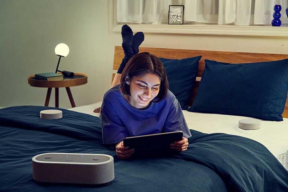 : A girl laying down with a tablet in hand and HTAX7 home theatre speaker next to her.