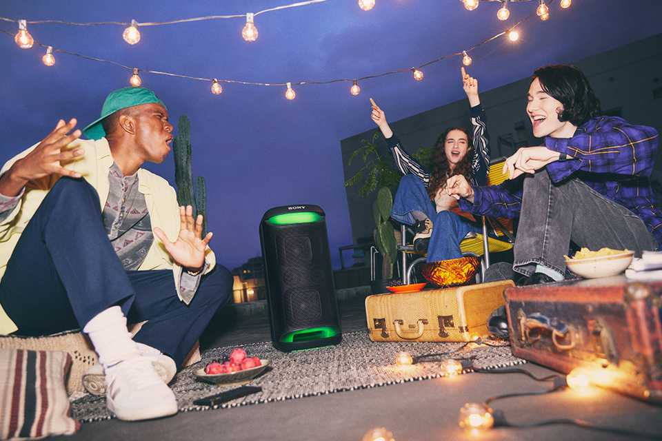 Three friends chilling in an outdoor location while listening to a Sony wireless party speaker.