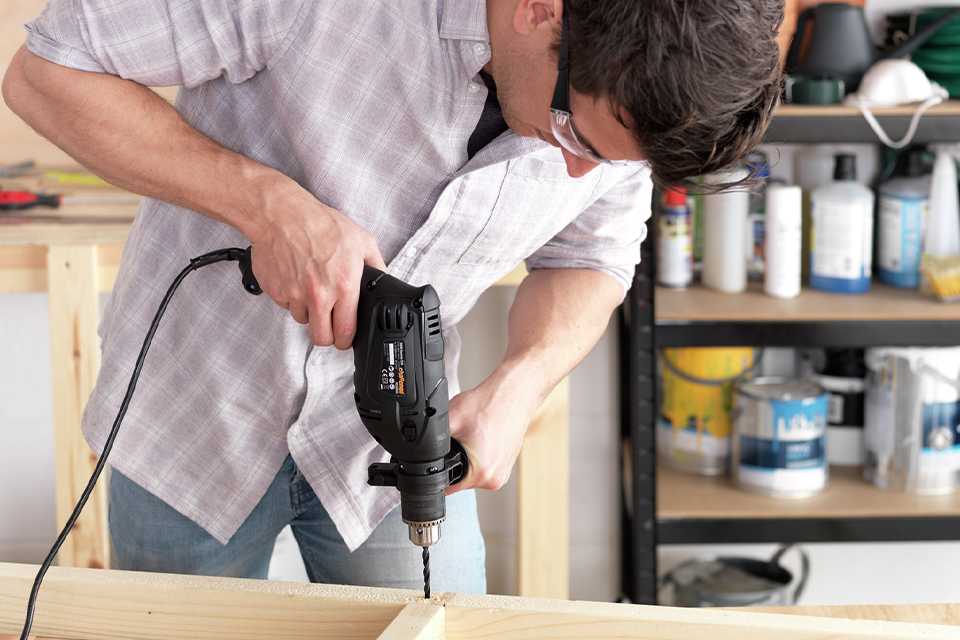 A man using a 500W Challenge corded impact drill to drill into a piece of wood.