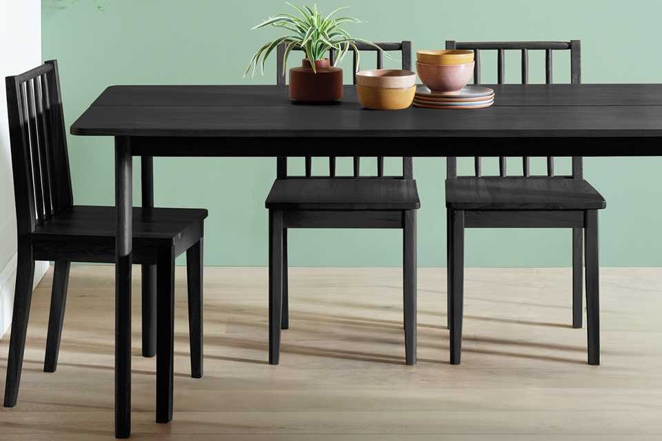 A Habitat Nel wood veneer black 4 seater dining table in a dining room with matching chairs placed around it.