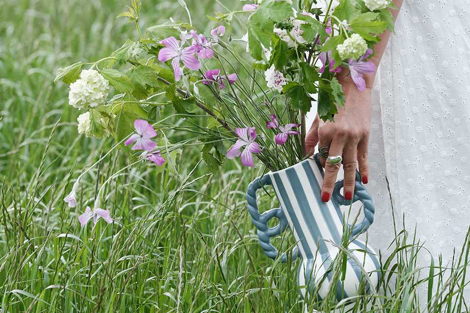 A woman holding a Habitat Stripe Ceramic Blue Vase with Wavy Handles and walking outdoors in tall grass.