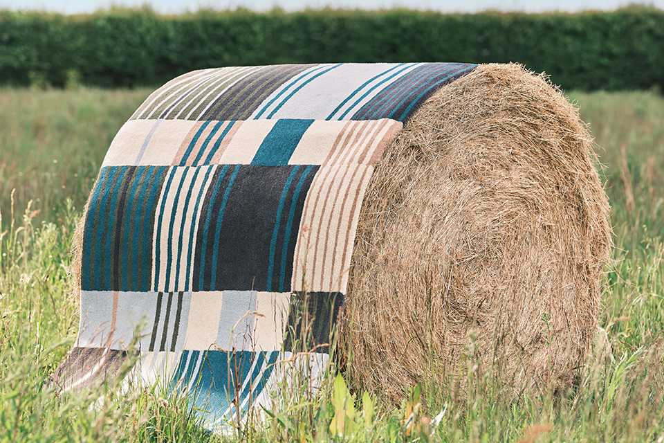A Habitat rug draped over a round hay bale.