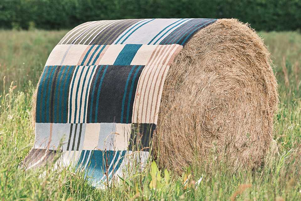 A Habitat rug draped over a round hay bale.