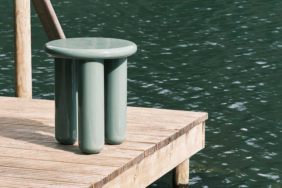 A Habitat side table in green colour placed on a lakeside deck.