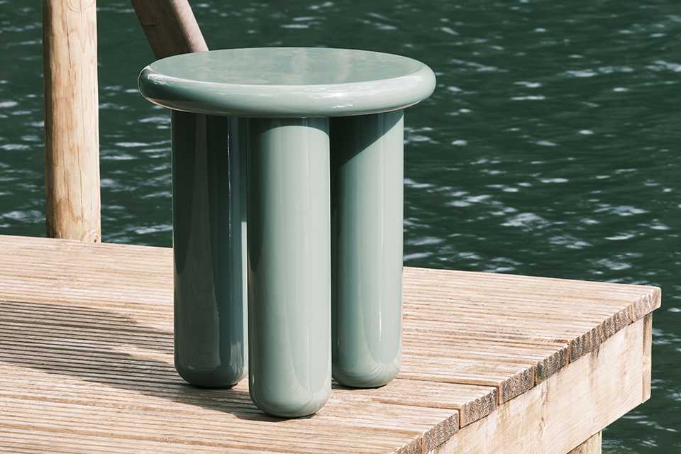 A Habitat side table in green colour placed on a lakeside deck.