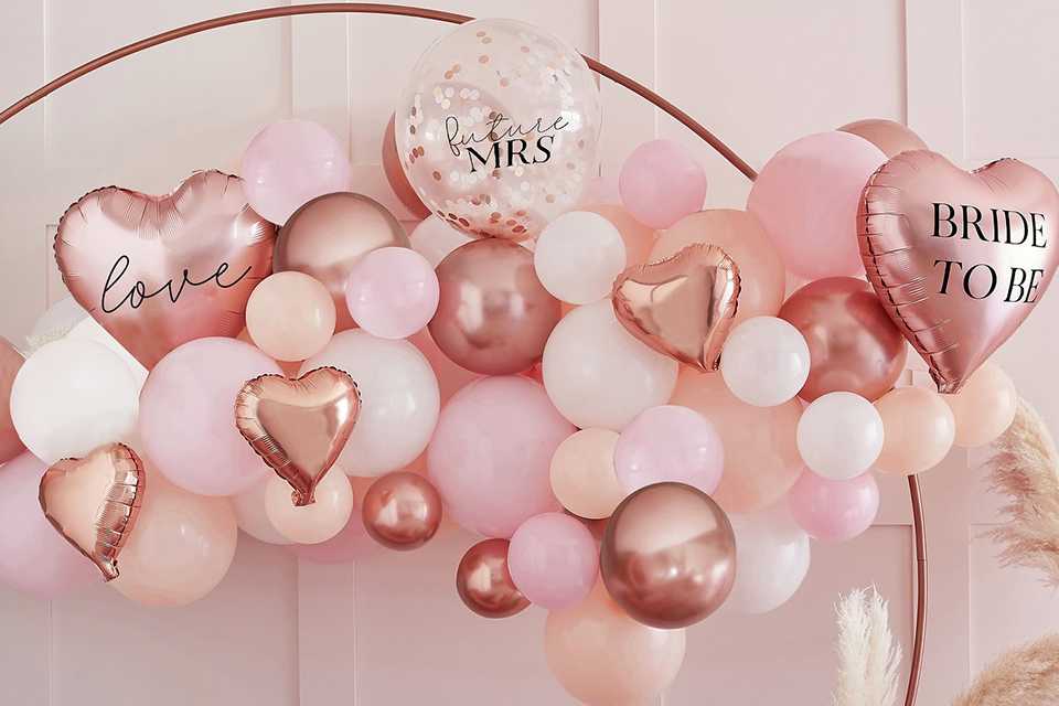 Ginger Ray Hen Party Confetti Balloon Arch set up over a pink sofa.