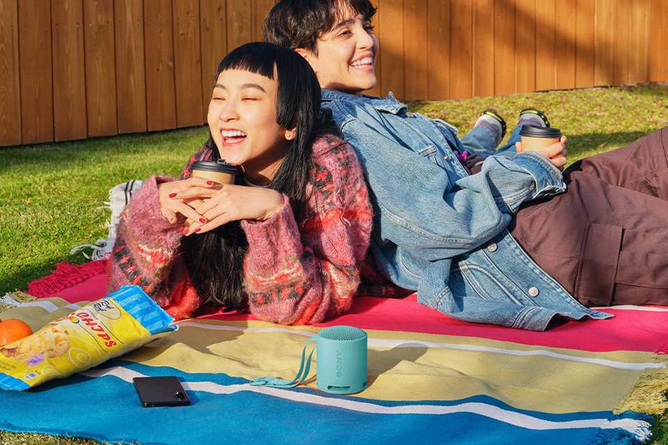 Sony SRS-XB100 Bluetooth Portable Speaker in black colour placed outdoors on a rug.
