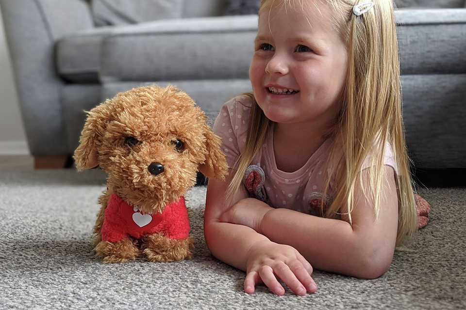 A girl smiling next to a Walkies with Waffle the Wonder Dog Soft Toy.
