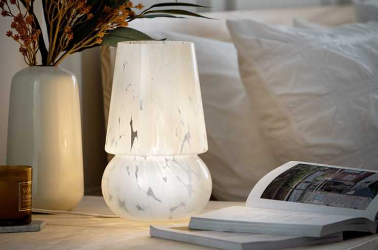 A white Habitat Rahnn confetti glass table lamp placed on a bedside table with other things.