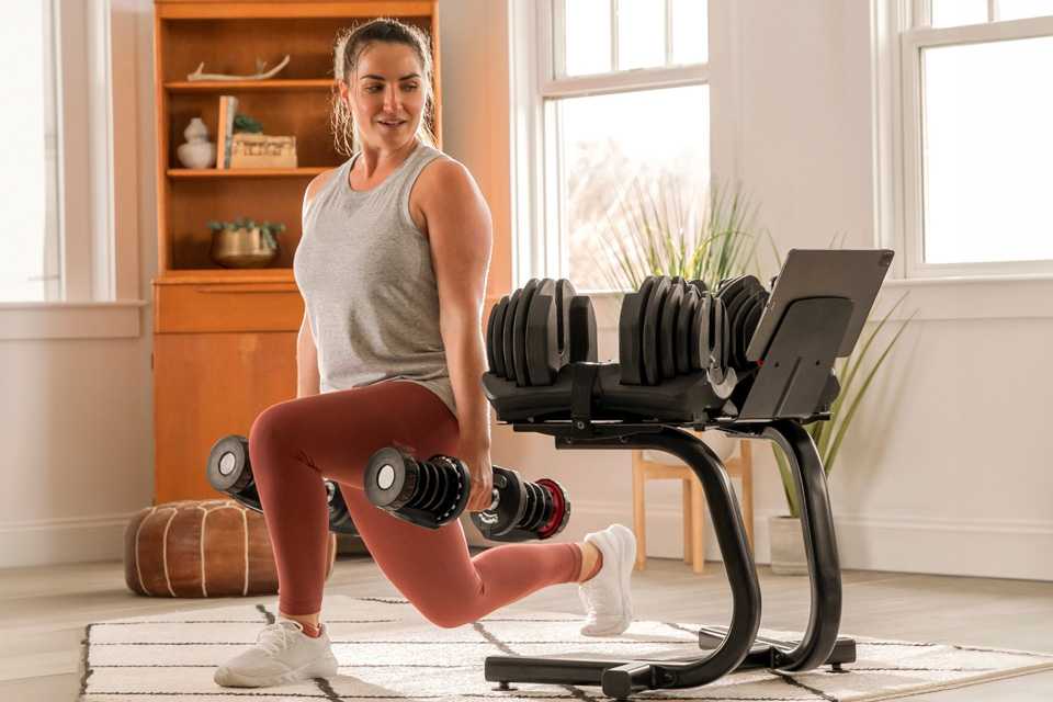 A woman using BowFlex SelectTech Stand with Media Rack to workout at home.