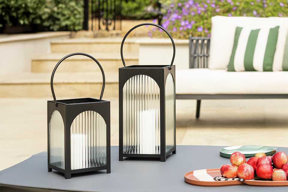 A pair of Habitat Hurricane Lantern in small and large sizes placed on a outdoor coffee table.