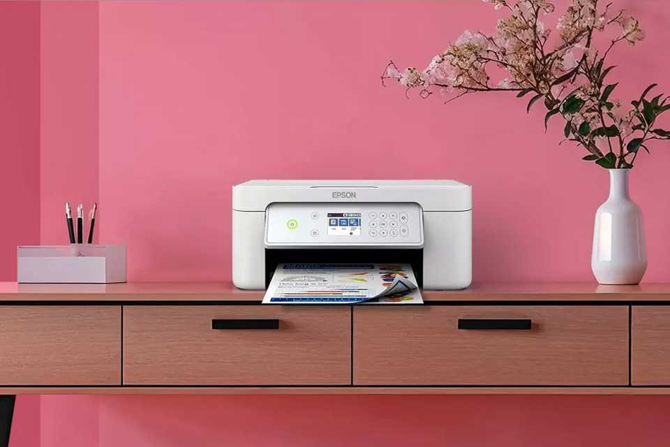 A white Epson printer placed on a table against a pink wall.