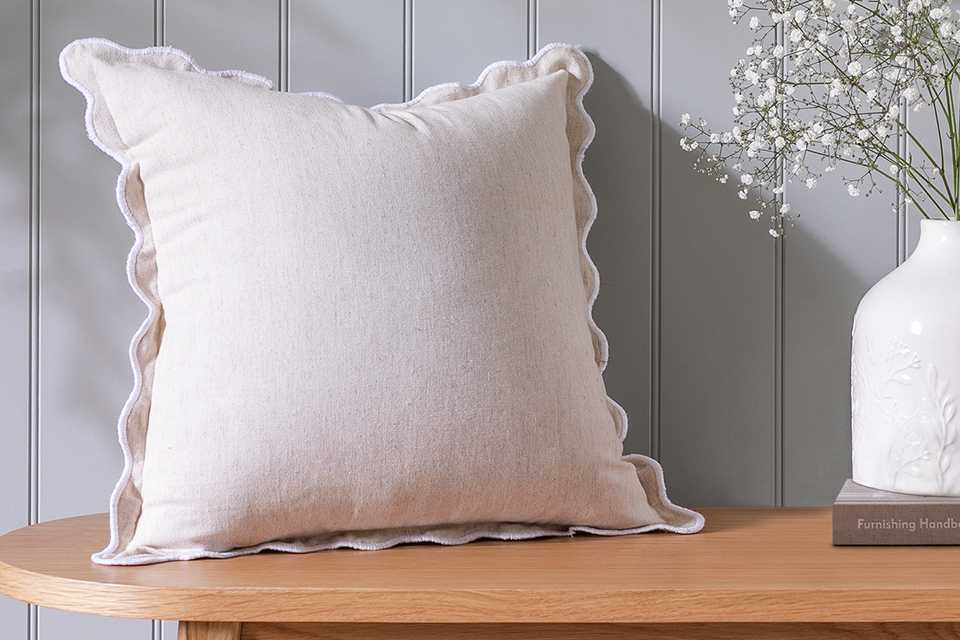 Habitat scalloped white natuiral cushion on wooden bench withvase and flowers.