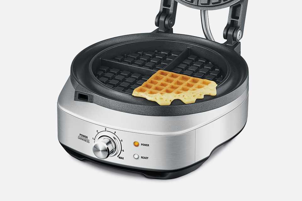 An open Sage No-Mess Waffle Maker with piece of waffle inside.
