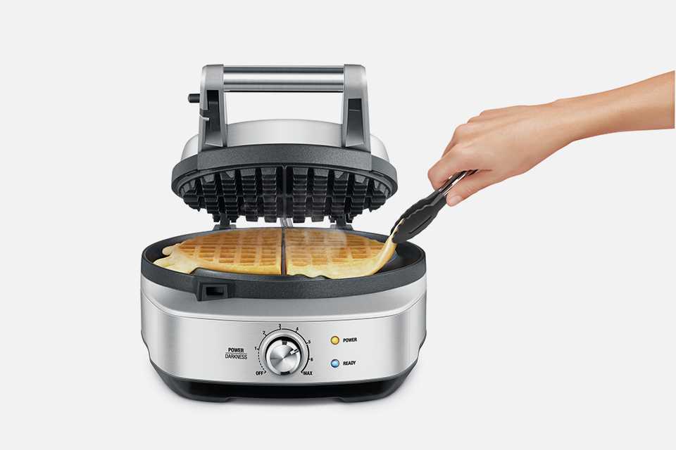 An open Sage No-Mess Waffle™ Maker with waffle cooking inside.