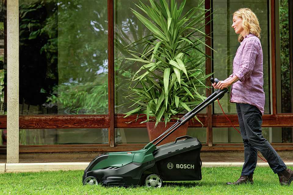 Blond woman in pink shirt mowing the grass with a Bosch lawnmower
