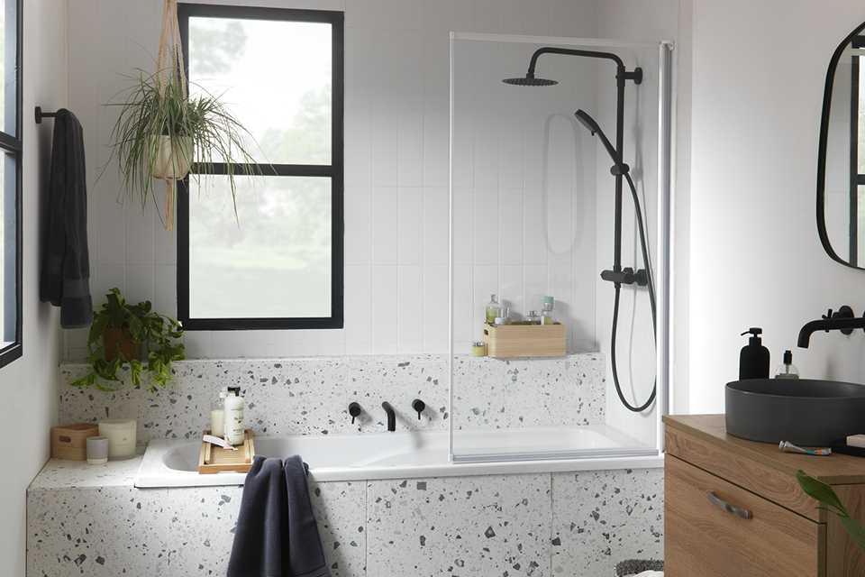 A white bathroom with a 3mm Fully Framed Bath Screen, wooden under-sink storage and black fittings.