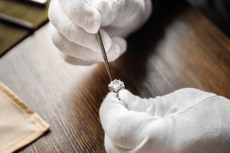 A person wearing gloves repairing a stone from a piece of jewellery.