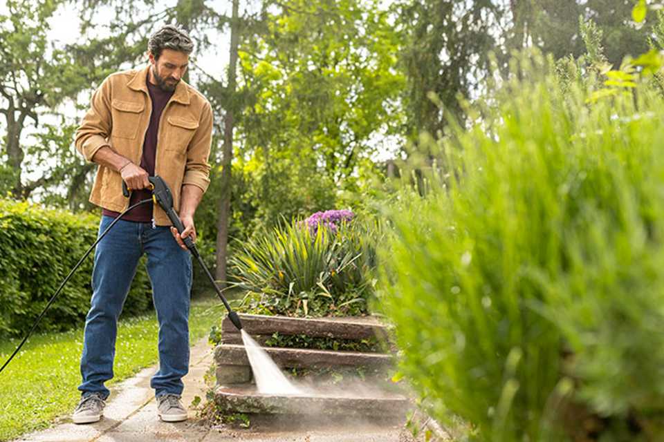 A man using Kärcher pressure washer against a garden pavement.