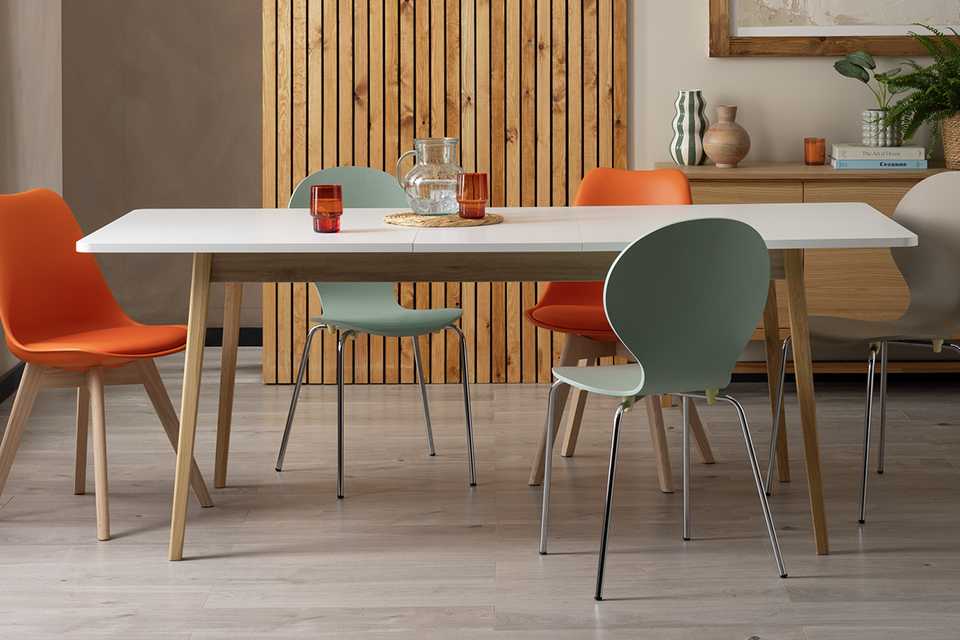 A Habitat Sylas Extending 6-8 Seater Dining white Table with orange chairs in a dining room.