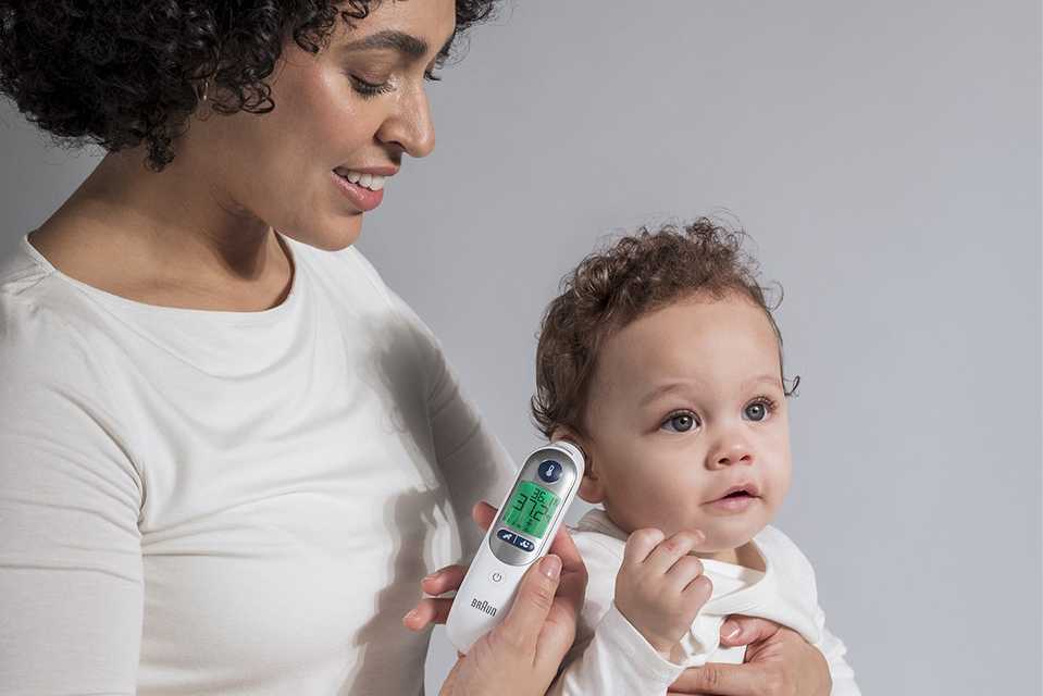 A mother checking her baby's temperature with Braun IRT6525 ThermoScan 7+ Ear Thermometer with Night mode.