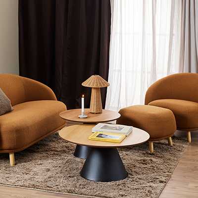 A round coffee table in natural and black colour in front of a sofa.