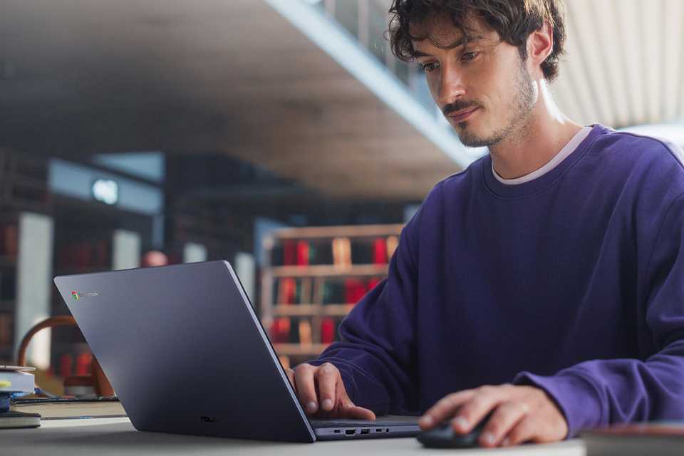 A man wearing purple T-shirt using ASUS CX1405CTA 14in i3 8GB 12GB Chromebook Plus.