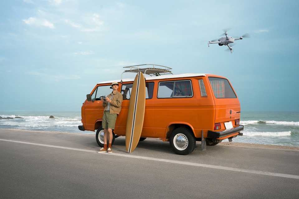 A man using a DJI Lito X1 Fly More 33MP camera drone outside his van near a seashore.
