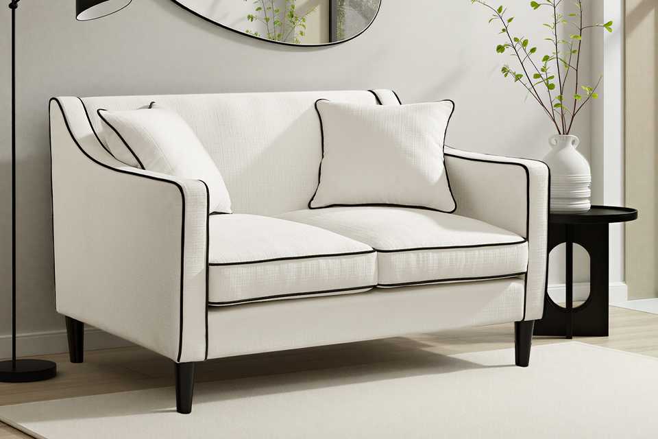 A white two seater sofa with black borders in a living room.