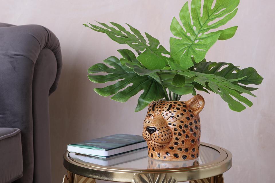 An artificial plant in a leopard head planter on a side table.