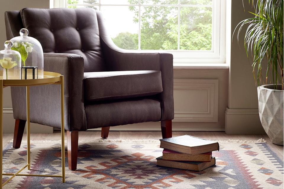 A comfy armchair positioned by a window on top of a brightly patterned rug.