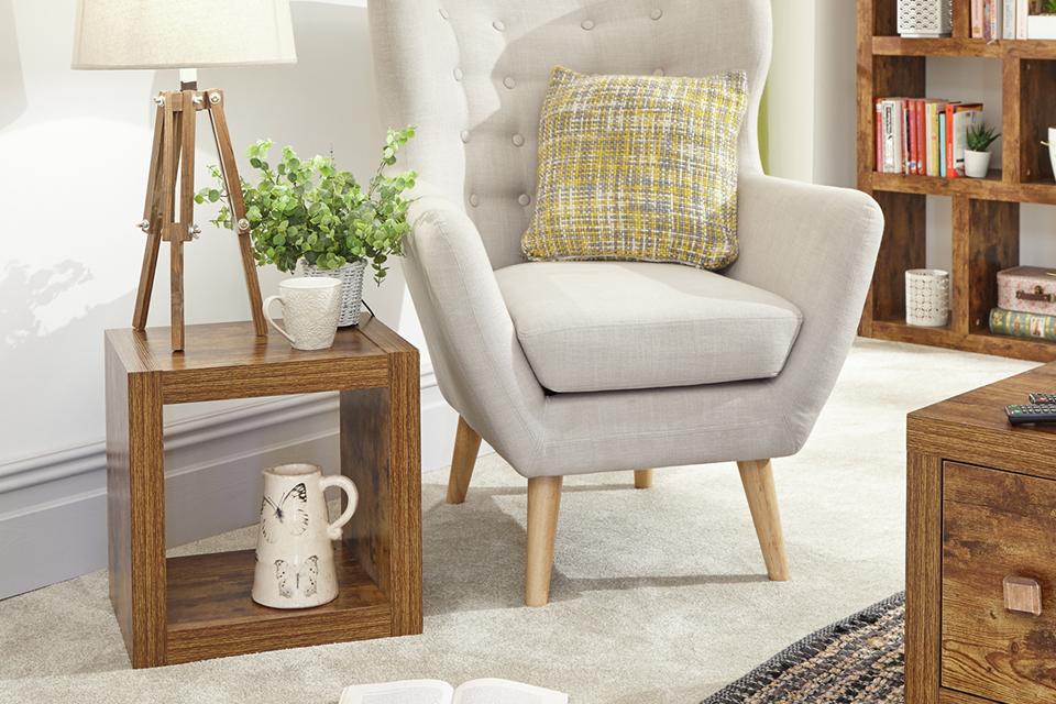 A cube side table decorated with ornaments and a lamp beside an armchair.