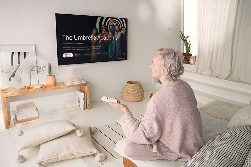 A woman sitting on a bed using Google Chromecast on a TV.