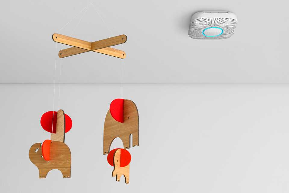 Google Nest smoke and CO detector attached to the ceiling adjacent to a cot mobile.