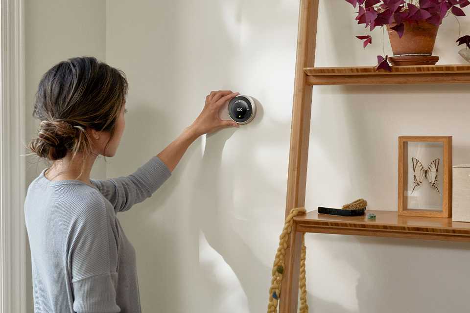 A woman setting up a Google Nest thermostat at her home.