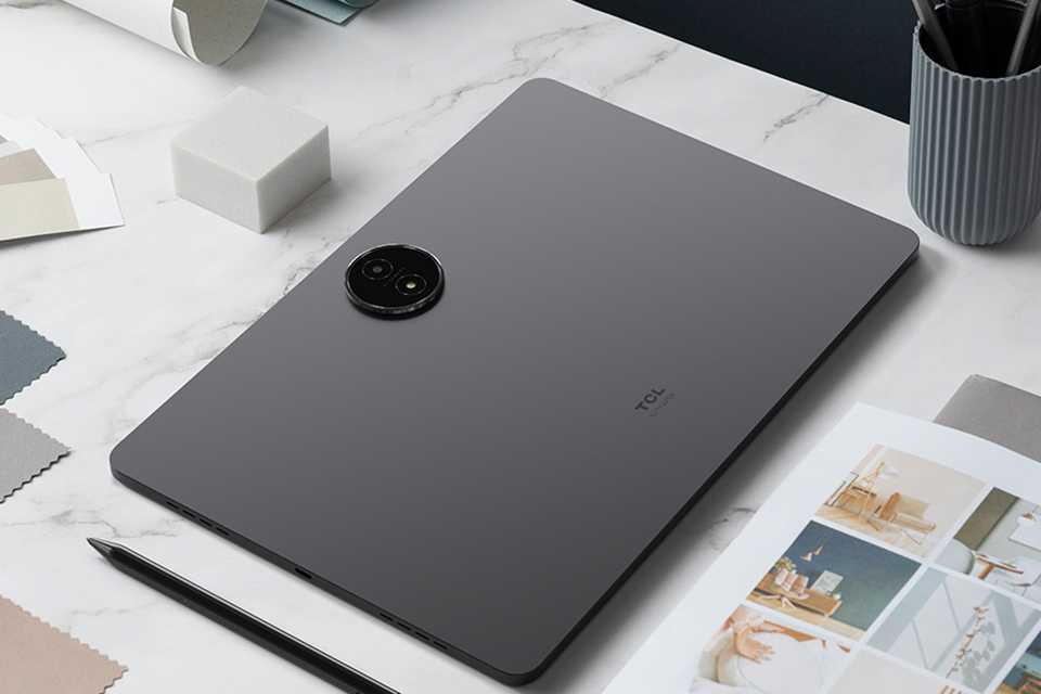 A grey TCL NXTPAPER 14 256GB Wi-Fi tablet placed on office desk with other things.