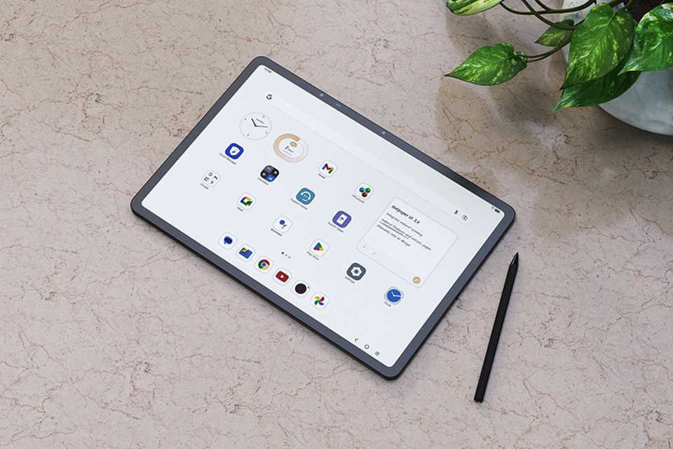 A grey TCL NXTPAPER 14 tablet with T-pen placed on a desk next to a potted plant.