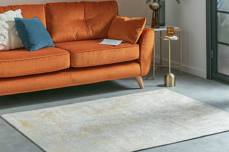 A Habitat distressed abstract gold flatweave rug placed in front of a sofa in a living room.