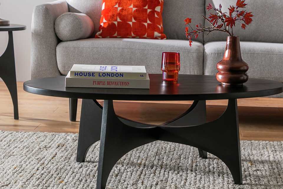 A flower vase, books and a glass on a Habitat Mid Century Round Coffee Table - Black.