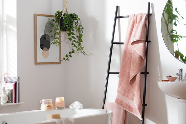 A picture frame, artifical plants, a bathtub and a towell ladder in a white bathroom.