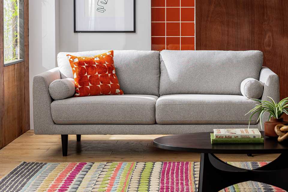 An orange cushion on a grey sofa in a living room.