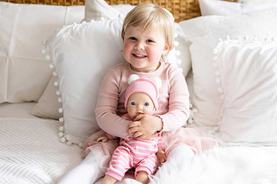 Toddler cuddling 36cm My First Tiny Treasures baby doll on bed.