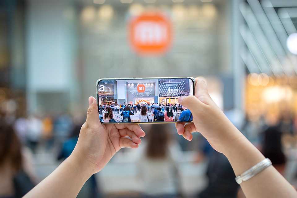 Hands holding a smartphone camera taking photo of a Xiaomi store.